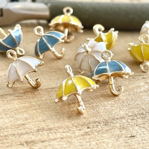 May include: Assortment of colourful enamel umbrella charms with gold accents. The charms are in shades of yellow, blue and white.