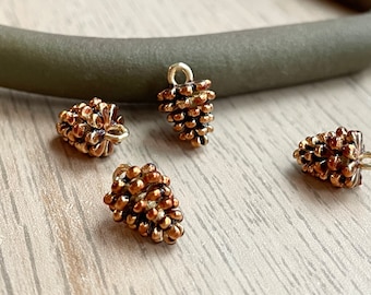 May include: Four gold-toned pine cone charms with a textured surface. The charms are small and have a loop at the top for attaching to jewellery or other crafts.