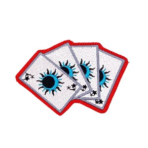 May include: Embroidered patch featuring four playing cards with a sun and eye design. The cards have a white background, a red border, and a blue and black sun design. The patch is suitable for jackets, bags, or other fabric items.