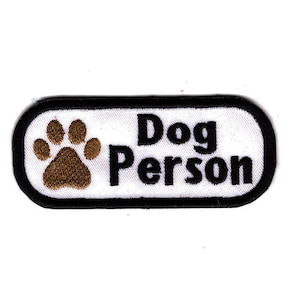 May include: White oval-shaped patch with black stitching around the edges. The patch has a brown paw print and the text "Dog Person" in black.