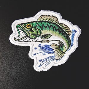 Op de afbeelding: Witte geborduurde patch van een groene en bruine baars die uit het water springt. Het water is afgebeeld met blauwe en groene borduurwerk.