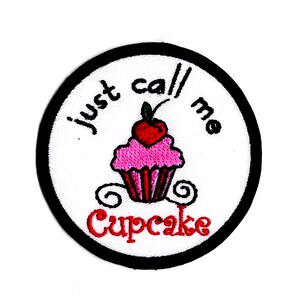 Peut inclure: Écusson brodé avec une bordure noire et un fond blanc. Le patch présente un cupcake rose avec une cerise rouge sur le dessus. Le texte "just call me Cupcake" est brodé autour du cupcake.