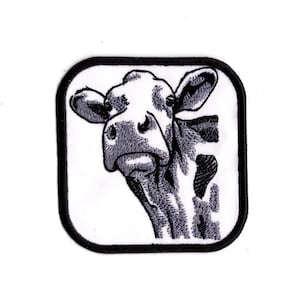 May include: Black and white embroidered patch of a cow's head with a black outline. The cow is looking to the left of the image.