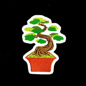 May include: A white embroidered patch of a bonsai tree with green leaves and a brown trunk in an orange pot.