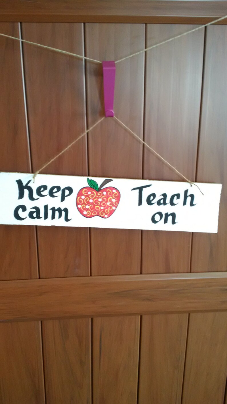 May include: A white wooden sign with the text "Keep Calm Teach On" and a red apple with yellow and white swirls painted on it.