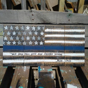 May include: Wooden sign with an American flag design, a blue line, and the quote "Well done thou good and faithful servant" with the scripture reference "Matt. 25:21".