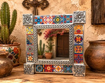 May include: A square mirror featuring a frame decorated with colorful Talavera-style ceramic tiles in shades of red, blue, yellow, and orange. The frame includes embossed silver-toned metal corners and a textured inner border surrounding the glass.