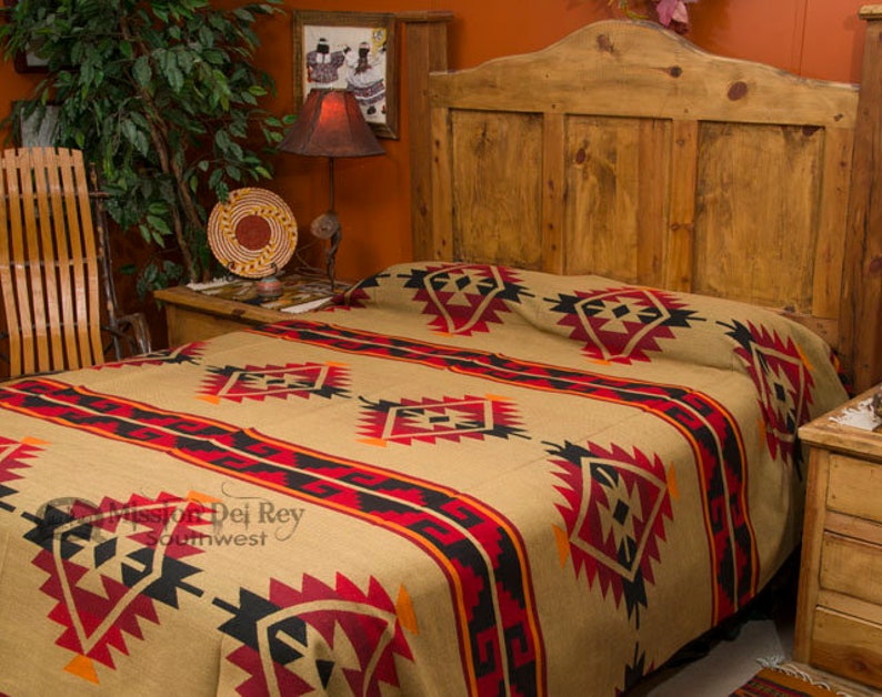 May include: A tan, red, black, and orange Southwestern-style throw blanket with geometric patterns is draped over a wooden bed frame. The blanket is made of a soft, woven fabric and features a traditional design.