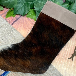 May include: A brown and white cowhide stocking with a light brown suede cuff and a green drawstring.