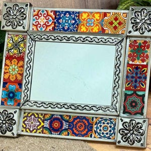 May include: Decorative rectangular mirror with a silver frame and colorful tile accents. The tiles feature intricate patterns in red, blue, orange, and yellow. The corners have decorative silver floral accents.