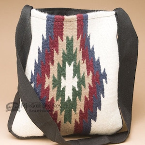 May include: A white woven bag with a geometric pattern in shades of red, green, blue, and brown. The bag has a black strap and is made of wool.