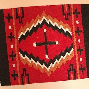 May include: A red, black, and white woven rug with a geometric pattern. The rug has a fringe border.