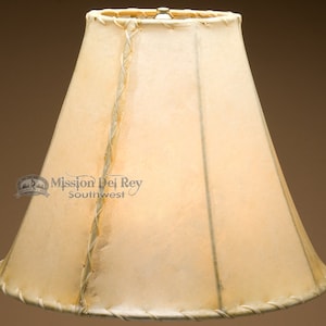 May include: A white leather lampshade with a braided leather trim. The lampshade is a cone shape and has a light brown background.