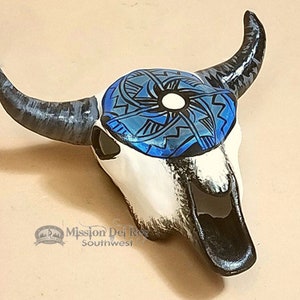 May include: A white ceramic bull skull with black horns and a blue and black geometric design painted on the forehead.