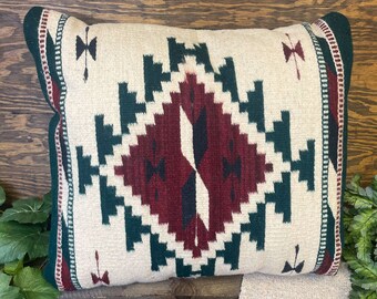 May include: A decorative pillow with a geometric pattern in shades of red, green, and white. The pillow has a fringed border and is made of a soft, woven fabric.