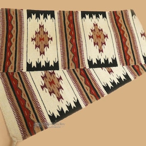 May include: A white, black, red, and brown woven rug with geometric patterns. The rug is folded in half and has fringe on the ends.