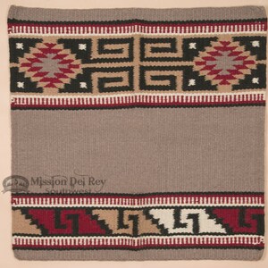 May include: A rectangular woven textile in shades of gray, tan, black, and red. The top and bottom borders feature geometric patterns, including diamond and stepped designs. The center is a solid gray field. The textile is likely a rug or blanket.