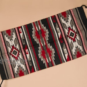 May include: A black, red, white, and gray woven rug with a geometric pattern. The rug has a fringe on the ends.