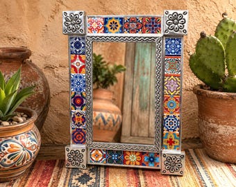 May include: A rectangular mirror featuring a silver metal frame decorated with colorful, patterned ceramic tiles in shades of blue, red, yellow, and orange. The four corners of the frame are accented with embossed silver floral metal squares.