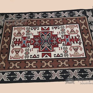 Peut inclure: Un tapis Navajo avec un motif géométrique traditionnel dans des tons de rouge, marron, blanc et noir. Le tapis présente une forme de diamant centrale avec des motifs géométriques plus petits qui l'entourent. Le tapis est bordé d'un motif géométrique noir et blanc.