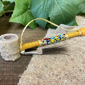 May include: A traditional Native American pipe made of bone and wood, decorated with colorful beads and a feather. The pipe is about 10 inches long and has a small bowl at one end.