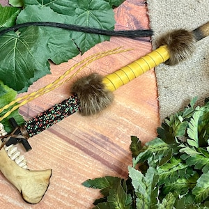 May include: A traditional Native American peace pipe with a bone mouthpiece, black and green beaded wrap, yellow leather wrappings, and a brown fur pom-pom.