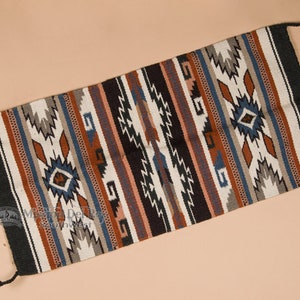 May include: A colorful woven rug with geometric patterns in shades of black, white, brown, blue, and red. The rug has a fringe on both ends.