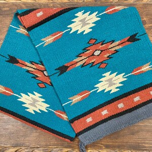 May include: A turquoise and red woven rug with a geometric pattern. The rug has a fringe on the bottom and is folded in half.
