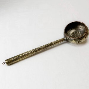 以下が含まれることがあります： 装飾的なハンドルが付いた銀色の金属製のレードル。レードルは、装飾的なデザインが施された丸いボウルを持っています。