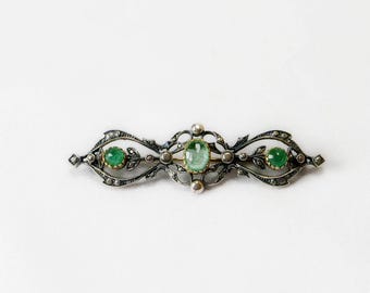Könnte beinhalten: Eine Brosche aus Silber und Gold mit drei grünen Edelsteinen, die in einem filigranen Blumenmuster gefasst sind.