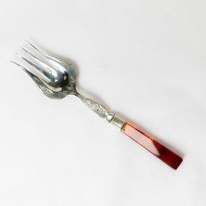 May include: A silver fork with an ornate design and a red and white handle.