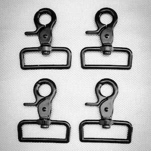 May include: Four black swivel snap hooks with rectangular loops and circular top rings. The hooks are made of metal and are arranged in a square pattern against a textured silver background. These are commonly used in bag making and crafting.