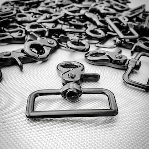 Könnte beinhalten: Nahaufnahme eines schwarzen Metall-Schnapphakens. Der Haken ist aus strapazierfähigem Metall gefertigt und hat eine glatte, polierte Oberfläche.