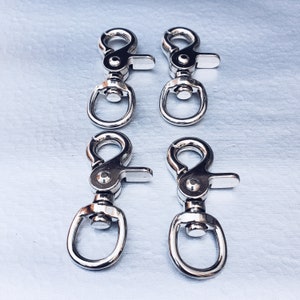 May include: Four silver metal swivel clasps with a spring-loaded gate. The clasps are commonly used for attaching leashes, keychains, or other items.