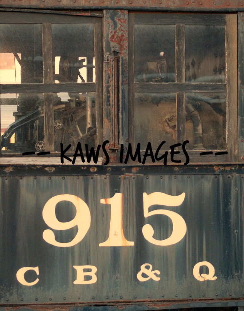 May include: A weathered, rusty, blue train car with the number 915 and the letters C B & Q painted in white on the side. The train car has a window with a view of the inside of the train.