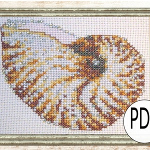 May include: Cross-stitch art of a nautilus shell in a distressed, light-colored wooden frame. The shell design features shades of brown, gold, and white, with small silver beads. A white circle with the letters "PDF" is in the lower right corner.
