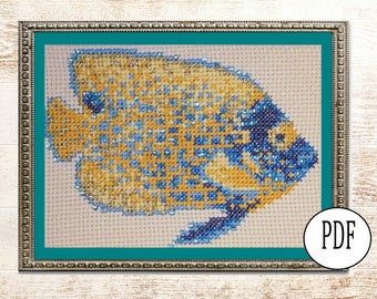 Pode incluir: Um padrão de ponto cruz de um peixe amarelo e azul com um design detalhado. O peixe está enquadrado em uma moldura prateada com um passe-partout turquesa.