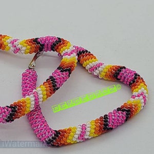 May include: A pair of heart-shaped hoop earrings. The earrings are beaded with a vibrant mix of colors, including pink, orange, yellow, white, and black. The earrings have a silver-colored clasp.