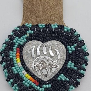 May include: A heart-shaped beaded keychain with a silver bear paw and bear design. The keychain features black, turquoise, and colorful beads, with a suede leather backing and a silver keyring.