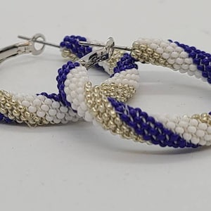 May include: A pair of hoop earrings with a beaded design. The earrings feature alternating sections of white, navy blue, and silver beads. The hoops have a silver clasp.