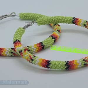 May include: A pair of beaded hoop earrings. The earrings are primarily light green, with sections of red, orange, yellow, black, and white beads. The hoops have silver-colored clasps.
