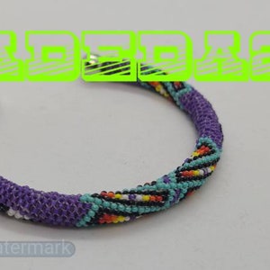 May include: A beaded bracelet with a purple base and a colorful pattern of turquoise, yellow, orange, and black beads. The bracelet has a silver-colored metal clasp. The word "BEADED" is in green text at the top.