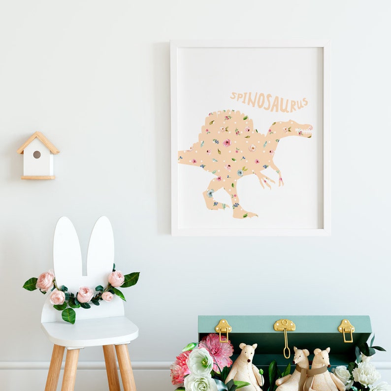 May include: A framed print featuring a Spinosaurus dinosaur silhouette filled with a floral pattern. The word "SPINOSAURUS" is above the dinosaur. A white bunny-eared chair with pink flowers and a small wooden birdhouse are also in the image.