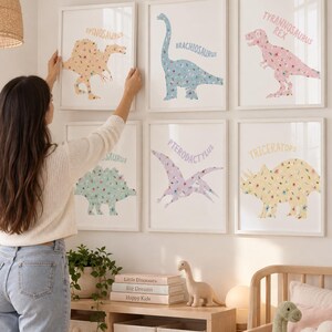 May include: Six framed wall art prints featuring floral-patterned dinosaurs including a Spinosaurus, Brachiosaurus, Tyrannosaurus Rex, Stegosaurus, Pterodactylus, and Triceratops, each labeled with its name in a soft-colored, sans-serif font.