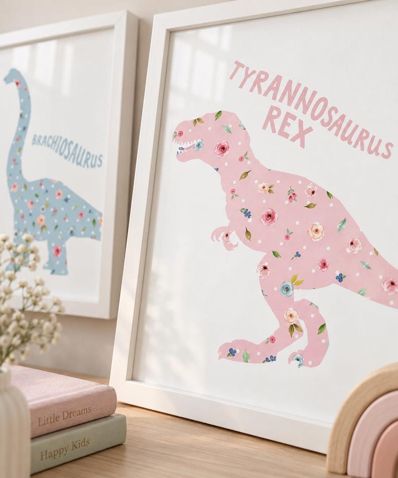 May include: A framed wall art print featuring a pink Tyrannosaurus Rex silhouette filled with a floral and white polka dot pattern. The text TYRANNOSAURUS REX is printed in pink above the dinosaur. A second framed print shows a blue Brachiosaurus.