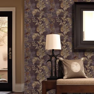Plum Damask Wallpaper with antique gold floral sprays and curling botanical leaves on a distressed aubergine background, shown in an entryway with a wooden bench, dark framed mirror, and table lamp.