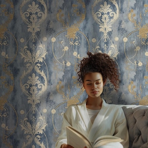 Blue damask wallpaper with a repeating vintage baroque pattern featuring ivory acanthus ornament, muted gold floral scrolls, and a distressed blue textured background, styled in a calm reading corner with soft upholstery and natural light.