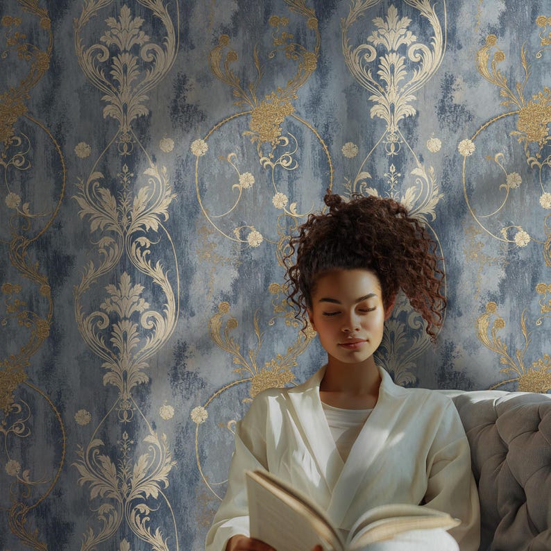 Blue damask wallpaper with a repeating vintage baroque pattern featuring ivory acanthus ornament, muted gold floral scrolls, and a distressed blue textured background, styled in a calm reading corner with soft upholstery and natural light.