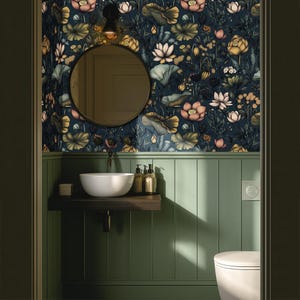 May include: A bathroom with a dark floral wallpaper featuring lotus flowers in shades of pink, yellow, and white against a navy blue background. The room has a round mirror, a white sink, and green paneling.
