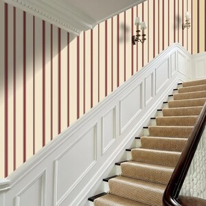 May include: A staircase with beige carpeted steps and a dark wooden handrail. The wall is painted with vertical stripes of cream and burgundy. White molding and sconces add architectural detail to the interior.
